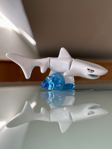 En hvid hajfigur med blå detaljer hviler på en blank overflade, reflekterende dens spejlbillede.