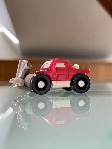 Rødt legetøjsbrandbil med bevægelige dele og sorte dæk, reflekteret på en blank overflade.